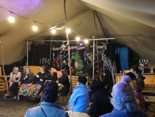 event attendees in an atmospheric festival space with engaging panellists and festoon lighting